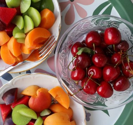 Vibrant mix of fresh summer fruits in decorative bowls on a floral patterned tray.