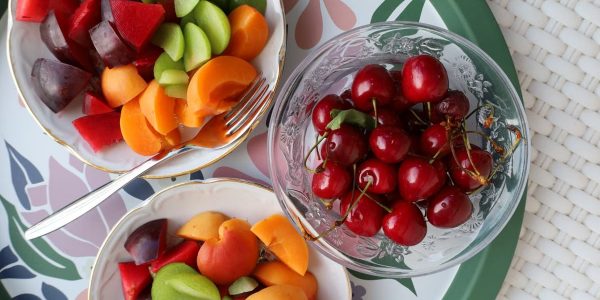 Vibrant mix of fresh summer fruits in decorative bowls on a floral patterned tray.
