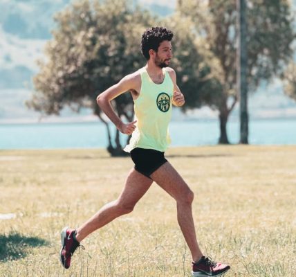 Side view of young determined male athlete in sportswear running on lawn in park near lake in sunny morning