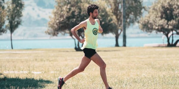 Side view of young determined male athlete in sportswear running on lawn in park near lake in sunny morning